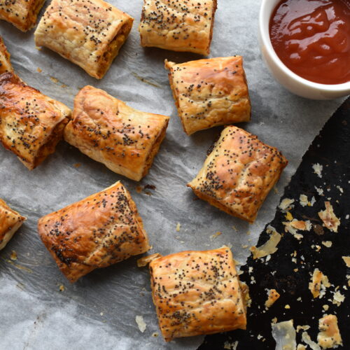 Vegan Sausage Rolls with Poppy seeds. On baking tray with tomato sauce and knife